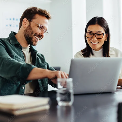 Deux collègues souriants travaillant ensemble sur un ordinateur portable dans un bureau.
