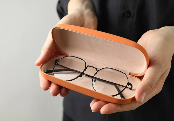 Mains tenant un étui à lunettes orange ouvert avec des lunettes à monture noire à Montrouge dans les Hauts-de-Seine 92