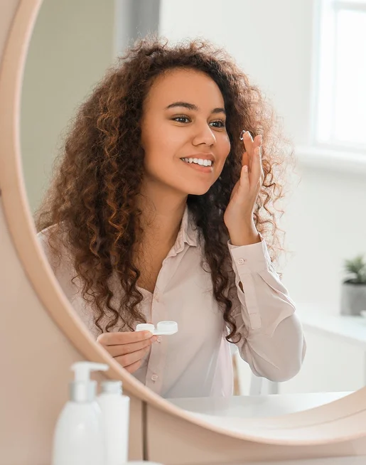 Jeune femme souriante mettant des lentilles de contact, vue dans un miroir à Montrouge dans les Hauts-de-Seine 92