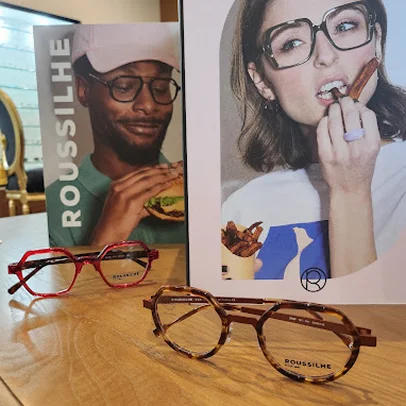Deux paires de lunettes devant des affiches publicitaires Roussilhe avec des personnes mangeant.